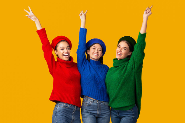 Positieve meisjes Gesturing V-teken glimlachen poseren over gele achtergrond - Foto, afbeelding