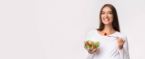 白い背景の上に立つ野菜サラダを食べる期待の女性,パノラマ - 写真・画像
