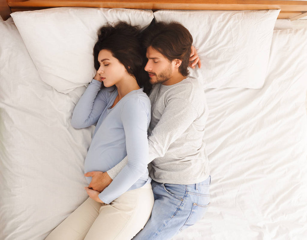 夫はベッドで寝ている間に妊娠中の妻を抱きかかえて - 写真・画像