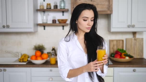 Young Cheerful Girl Holding A Glass Of Orange Juice On Kitchen. - Кадри, відео