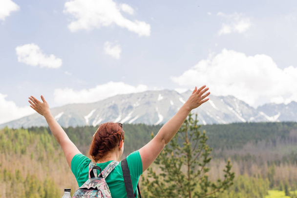 Udane młoda kobieta Backpacker otwarte ramiona na szczycie góry. Ładna ruda dziewczyna stoi na wiosennych śnieżnych górach. Trekking i koncepcja turystyki. Przestrzeń kopiowania - Zdjęcie, obraz