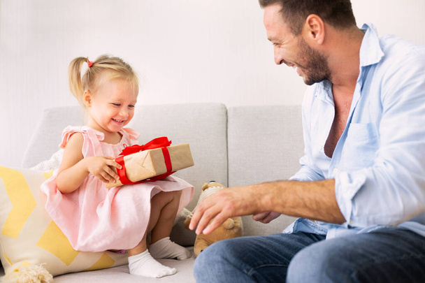 Emocionado chica sosteniendo su presente sentado con papá
 - Foto, imagen