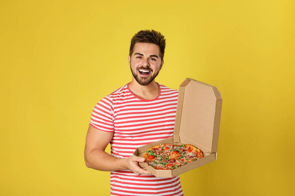 Handsome man with tasty pizza on yellow background - Foto, Bild