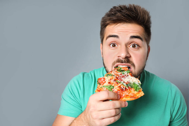 Handsome man eating pizza on grey background, space for text - 写真・画像