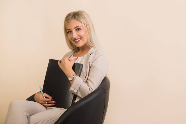 beautiful young woman in a suit with a folder on a beige background - Fotografie, Obrázek