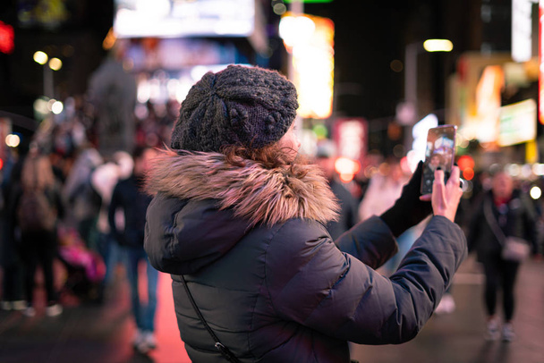 Piękna, kręcona brunetka robi sobie selfie swoim smartfonem na Times Square w Nowym Jorku. - Zdjęcie, obraz