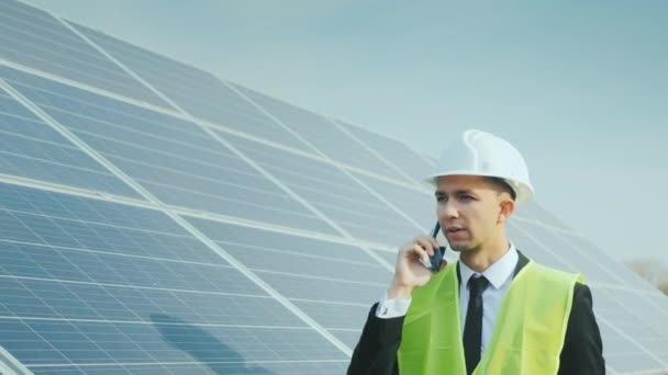 An engineer walks along the solar panels talking on the phone - Záběry, video