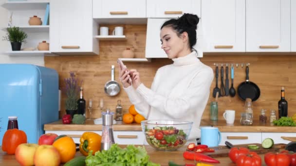 Mladá žena pomocí mobilního telefonu v kuchyni při vaření. - Záběry, video
