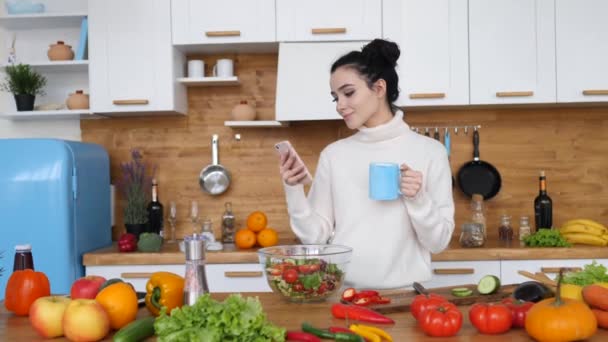 Young Woman Using Smartphone And Smiling In Kitchen - Filmagem, Vídeo