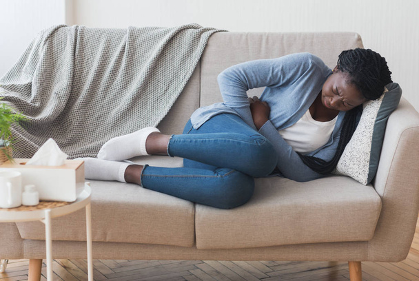 Chorą Afro dziewczynę leżącą na kanapie cierpiącą na ból brzucha - Zdjęcie, obraz