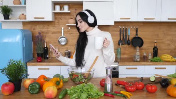 Woman Using Smartphone And Dancing In Kitchen Wearing Headphones. - Felvétel, videó