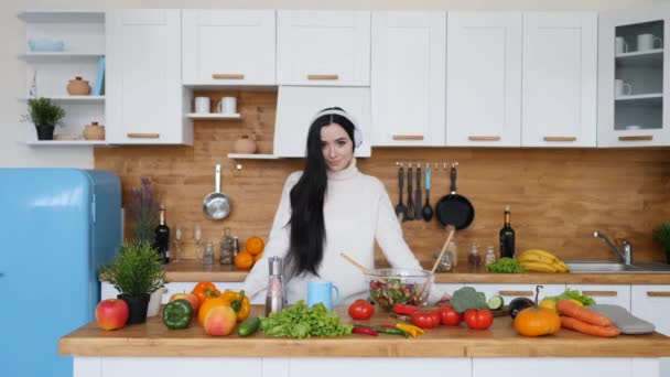 Portrait Of Young Brunette Woman Wearing Headphones Cooking On Kitchen. - Filmmaterial, Video