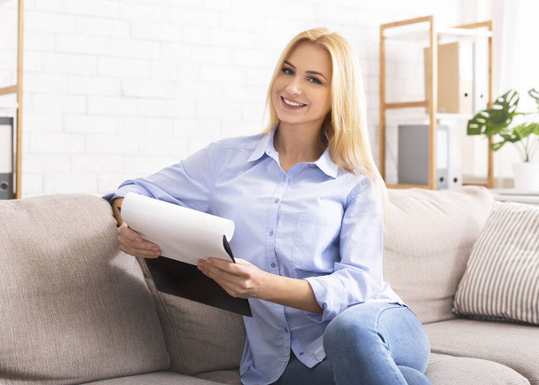 Cheerful female psychotherapist with clipboard sitting in office - Photo, Image
