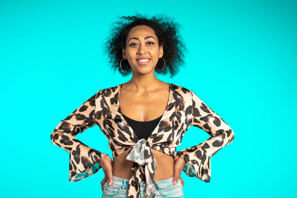 Pretty african woman with afro hair in leopard top smiling to camera over blue wall background. Cute mixed race girls portrait. - Foto, Imagem
