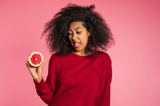 African american girl act ape her face from grapefruit cid. Woman grimaces. Lady with curly hairstyle on pink background. Diet. healthy lifestyle concept. - Foto, Imagem