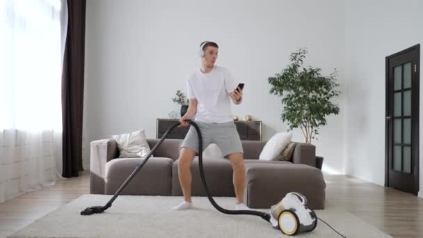 Young Man Having Fun Cleaning House With Vacuum Cleaner Dancing And Using Smartphone. - Video, Çekim
