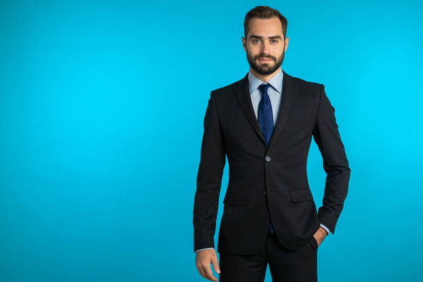 Copy space. Portrait of young successful confident businessman with beard isolated on blue studio background. Man in business suit looking to camera and smiling. Portraiture of handsome guy. - Foto, afbeelding