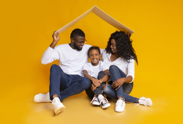 Adoptywni rodzice trzymający kartonowy dach nad małą czarną dziewczynką - Zdjęcie, obraz