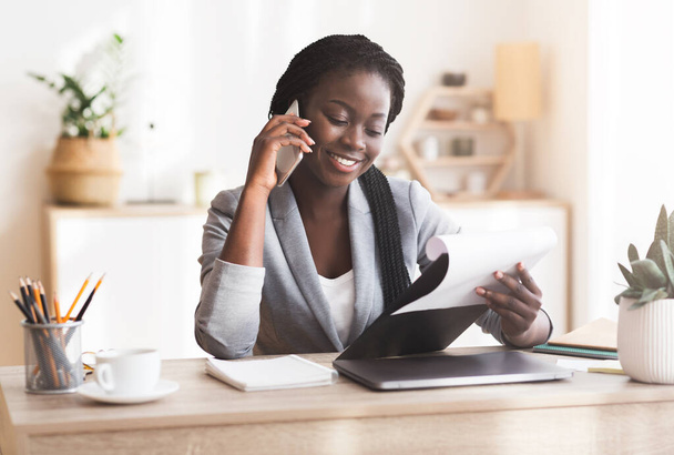 Zwarte vrouwelijke manager maakt telefoongesprekken en het controleren van rapporten in het kantoor - Foto, afbeelding