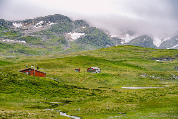 山小屋の木造山小屋はノルウェーを通ります。典型的な北欧の芝生の屋根の家とノルウェーの風景。谷の屋根の上に草の小さな家や木造キャビンと山の村 - 写真・画像