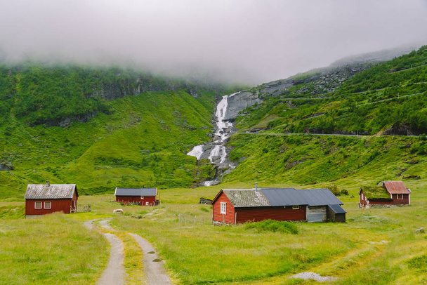 chaty drewniane schroniska górskie w przełęczy Norwegia. Norweski krajobraz z typowymi skandynawskimi domami z trawy. Górska wioska z domkami i drewnianymi domkami z trawą na dachu w dolinie - Zdjęcie, obraz