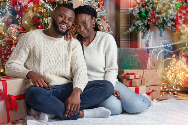Retrato de pareja negra romántica sentada en el suelo cerca del árbol de Navidad
 - Foto, Imagen