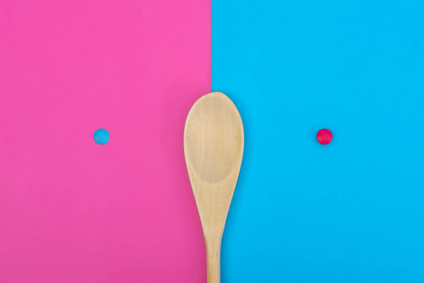 Blue pill on a pink background and a pink pill on a blue background. Wooden spoon on a two-tone background. The concept of various dietary supplements for diet control, flat lay - Photo, Image