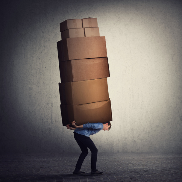 Bent down guy carrying a lot of big heavy boxes on his back. Ove - 写真・画像