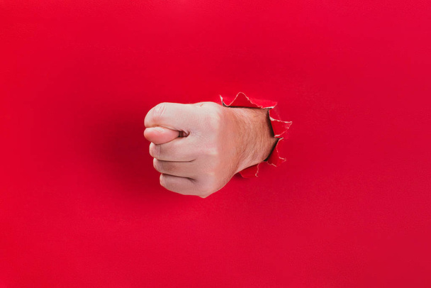 Male hand shows a gesture fig through a hole in red background. - Foto, afbeelding