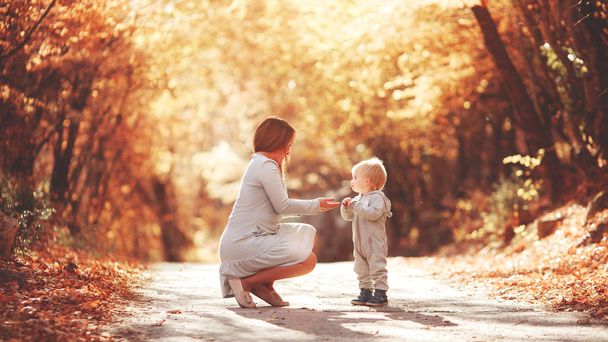 Young mother plays with her son in the autumn forest. Blond in a sports gray suit. Autumn leaves. Joyful family in nature. - Photo, Image
