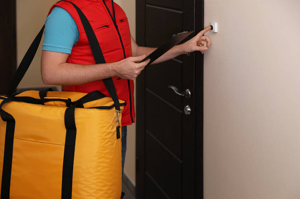 Male courier with thermo bag and clipboard ringing doorbell, closeup. Food delivery service - Foto, Imagem