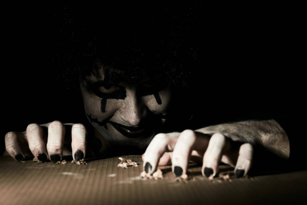 ein gruseliger Clown guckt aus dem Keller und kratzt mit seinen Krallen den Boden. - Foto, Bild