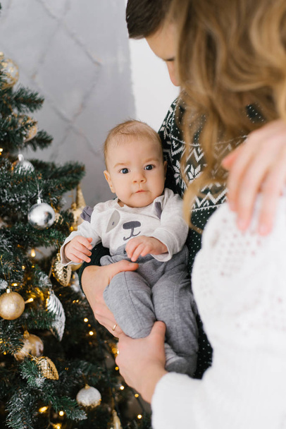 Little son of five months in his parents arms close up on the background of a Christmas tree - Φωτογραφία, εικόνα