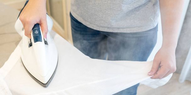 Panoram of Woman ironing sleeve of white shirt with much steam - Photo, Image