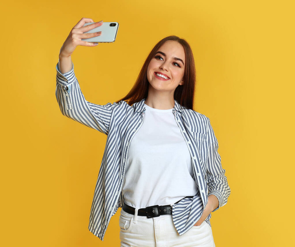 Young woman taking selfie on yellow background - Foto, afbeelding