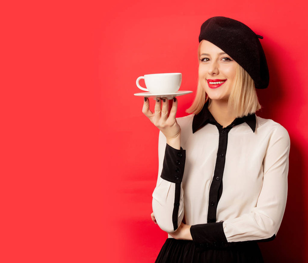 beautiful french woman in beret holds cup of coffee on red backg - Photo, Image