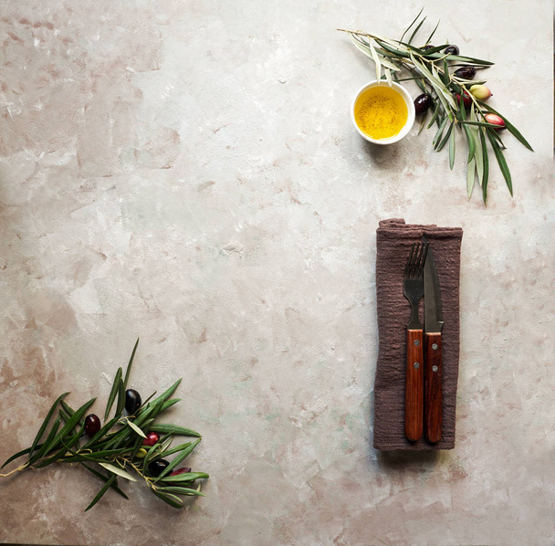 Lebensmittel Hintergrund mit Olivenzweig, Serviette und Teller, Messer und Gabel Besteck, Olivenöl auf Betongrund - Foto, Bild