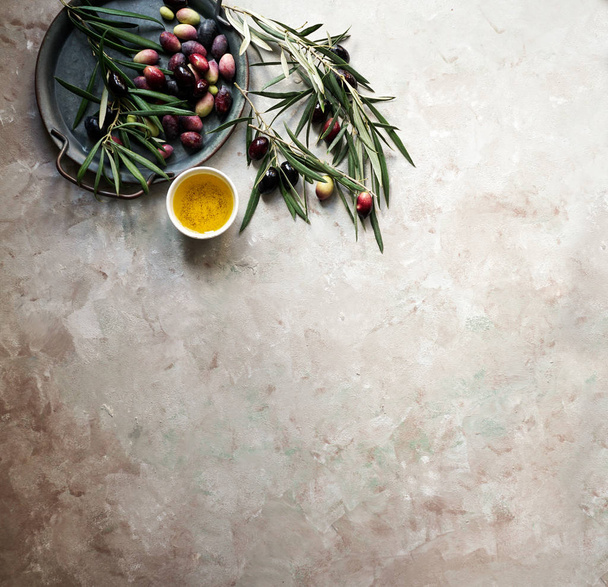 Food background with olive tree branch, napkin and plate, knife and fork cutlery, olive oil on concrete background - Foto, imagen