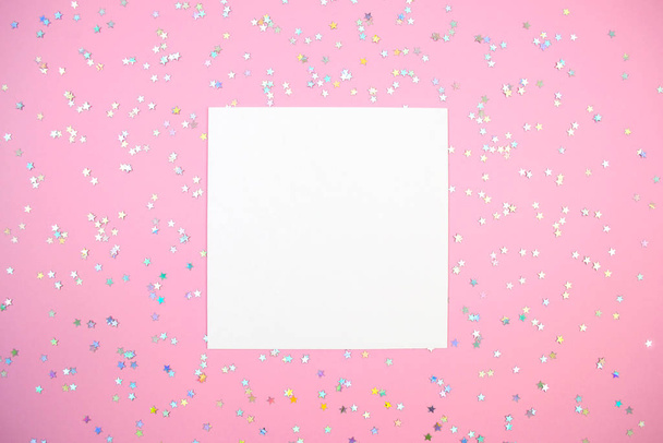 Empty white square paper card and holographic stars confetti flat lay on pink mock up - Foto, imagen