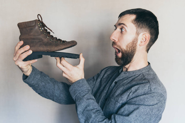 Man looking at an old leather boot with torn sole, surprise and shock on his face - Photo, Image