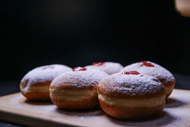 Hanukkah food doughnuts with jelly and sugar powder on black background. Jewish holiday Hanukkah concept and background. Copy space for text. Shallow DOF - Photo, Image
