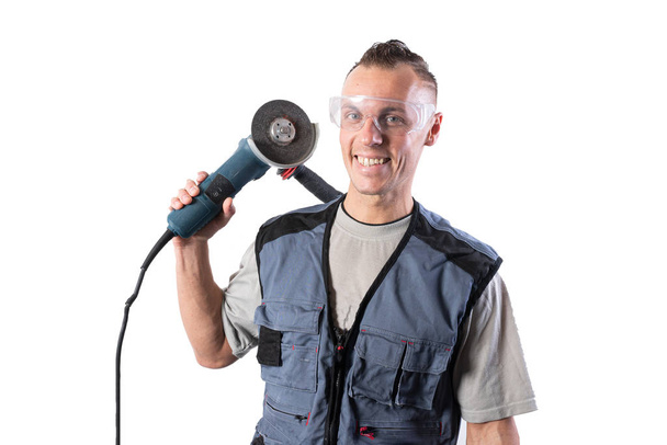 A builder in a helmet and a respirator, with an angle grinder on his shoulder. Smiles. - Photo, Image