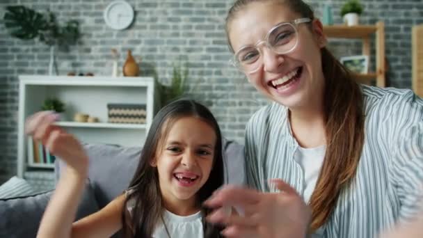 Joyful daughter and mother making video call from apartment waving hand smiling - Materiał filmowy, wideo