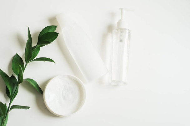 Means for skin care, rejuvenation and hydration of the face. Cream, micellar water and moisturizing lotion on a white background with a branch of green . The philosophy of self care and skin care - 写真・画像