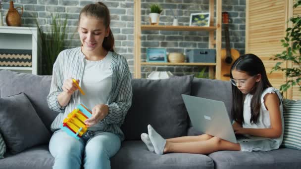 Funny adult woman playing with toy while serious daughter in glasses using laptop - Záběry, video