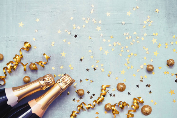Two champagne bottles and golden confetti on blue background. Flat lay of Christmas, New Year, Purim celebration concept. Copy space, top view. - Fotografie, Obrázek