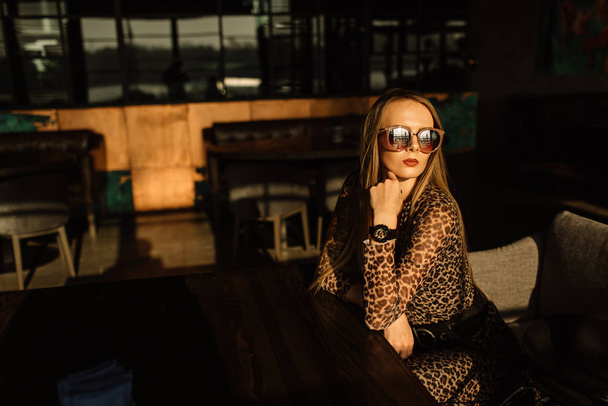 beautiful girl model in a restaurant in a beautiful loft interior. on the eyes of sunglasses, dressed in a leather black jacket, casual clothes. warm photography, sunlight - Zdjęcie, obraz