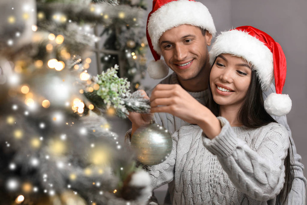 Happy young couple in Santa hats decorating Christmas tree toget - 写真・画像