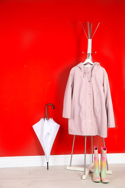 Stylish umbrella, raincoat and boots near red wall - 写真・画像
