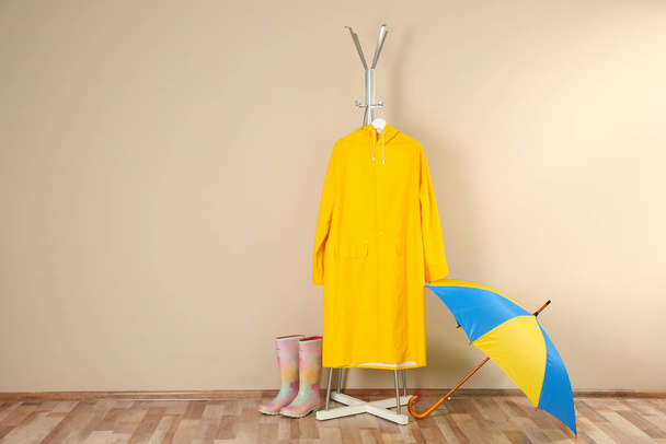 Umbrella, rain coat and rubber boots near beige wall. Space for text - Foto, Imagen